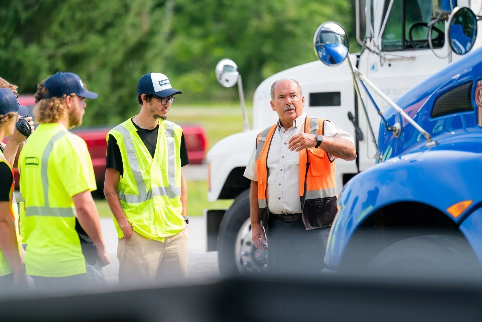 Three workers standing and talking in a parking lot of trucks.