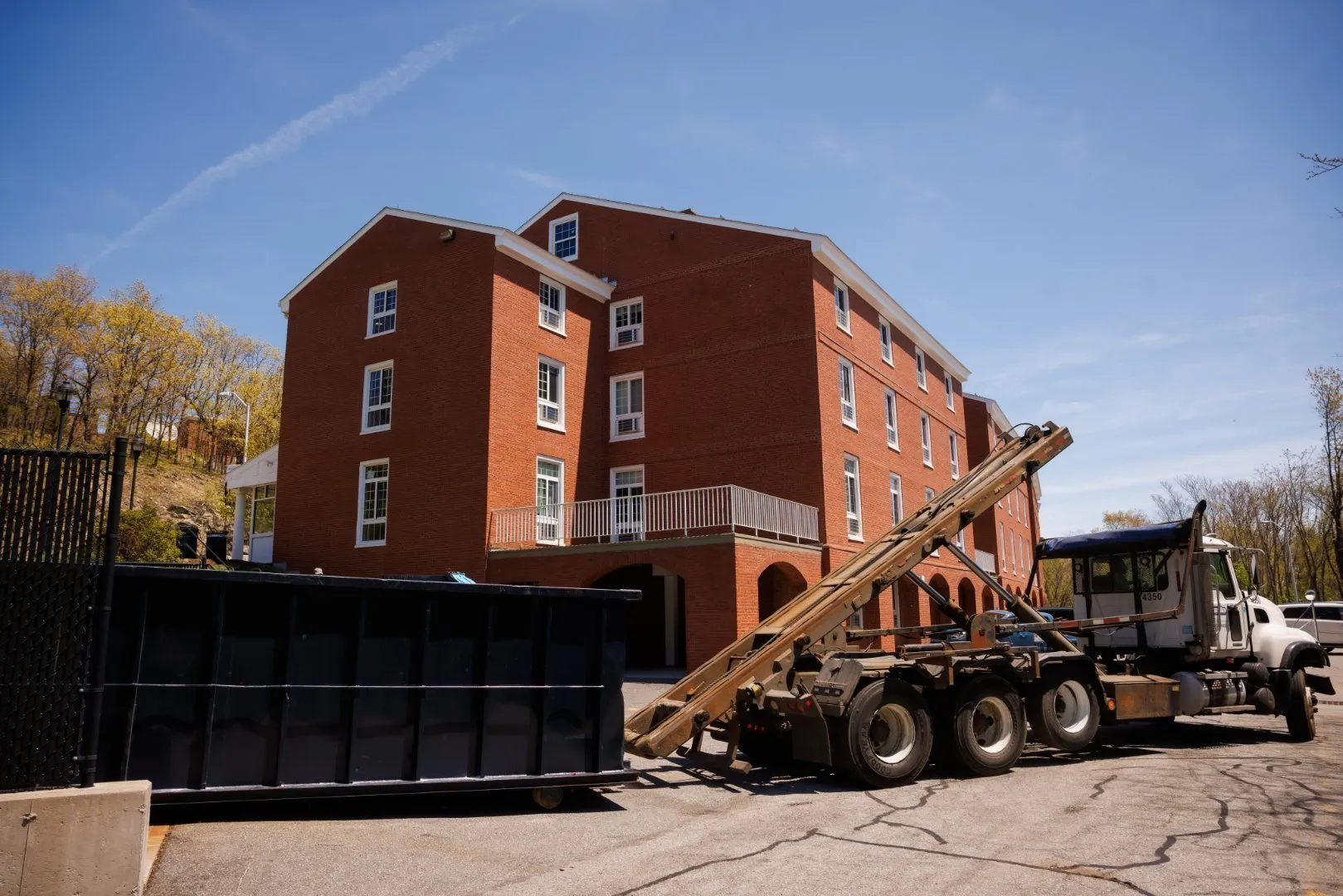 Casella roll-off truck servicing a dumpster outside a commercial brick building.