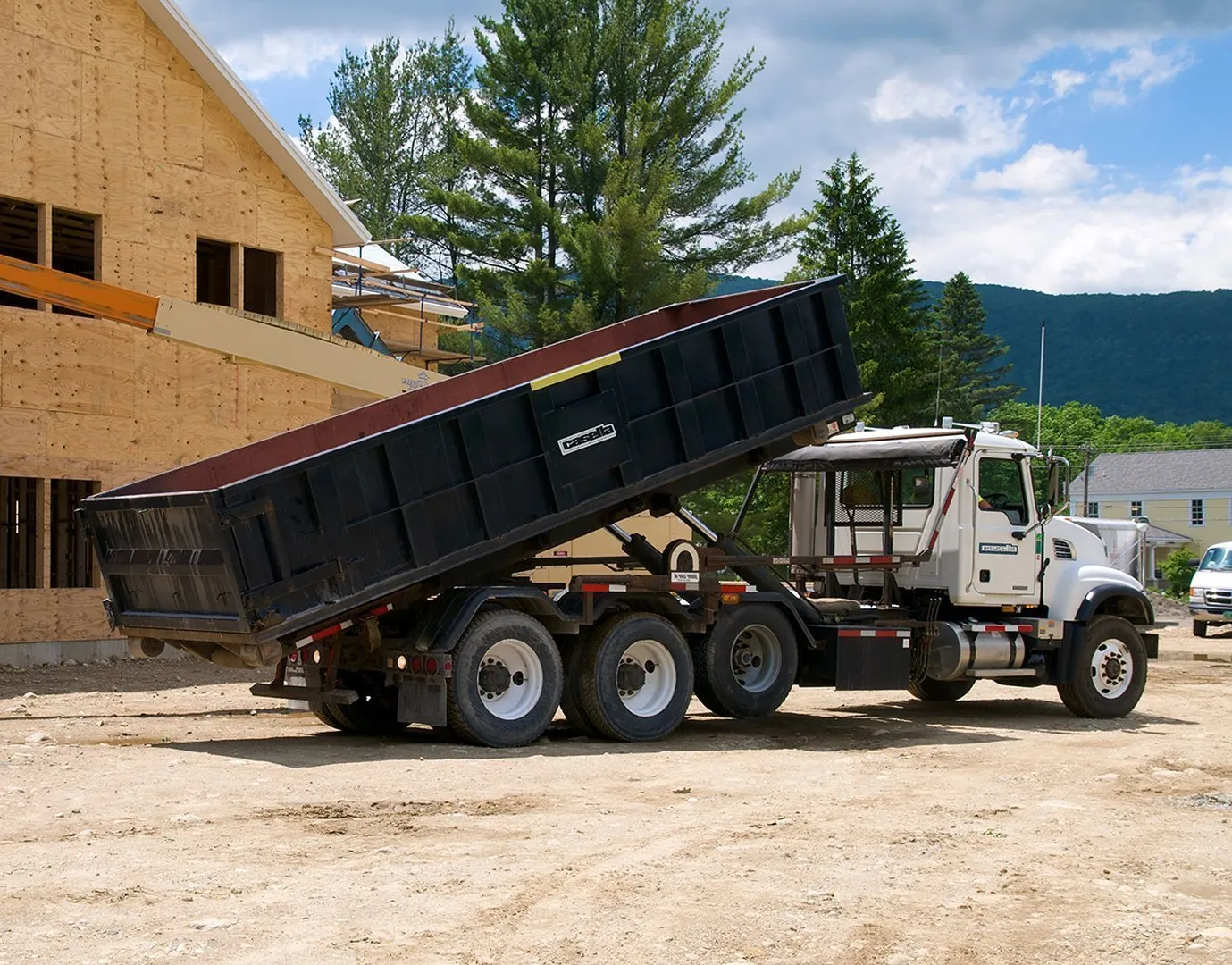 Casella roll-off truck unloading a container at a construction site near a partially built wooden structure. 