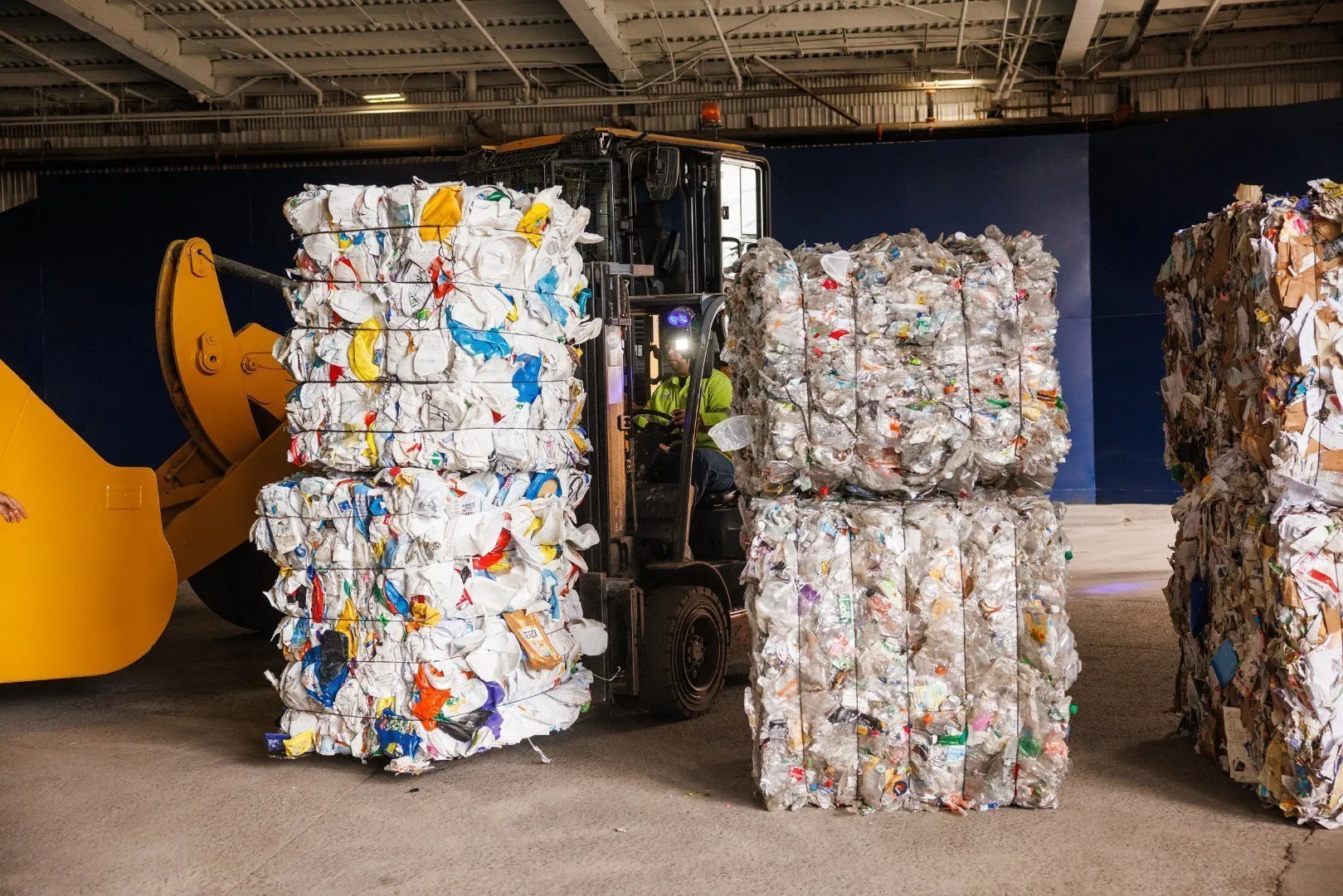 A worker operating a forklift moves large bales of compressed recyclable materials, in a recycling facility.