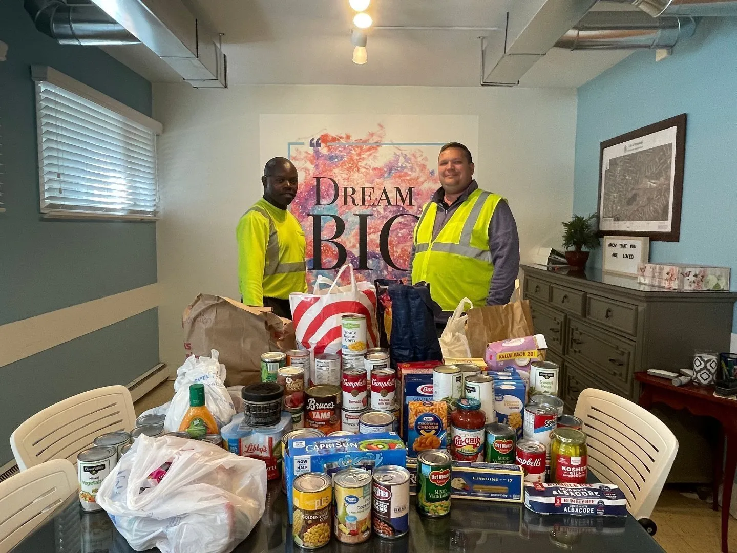 Two workers standing in an office with food donations on the table.