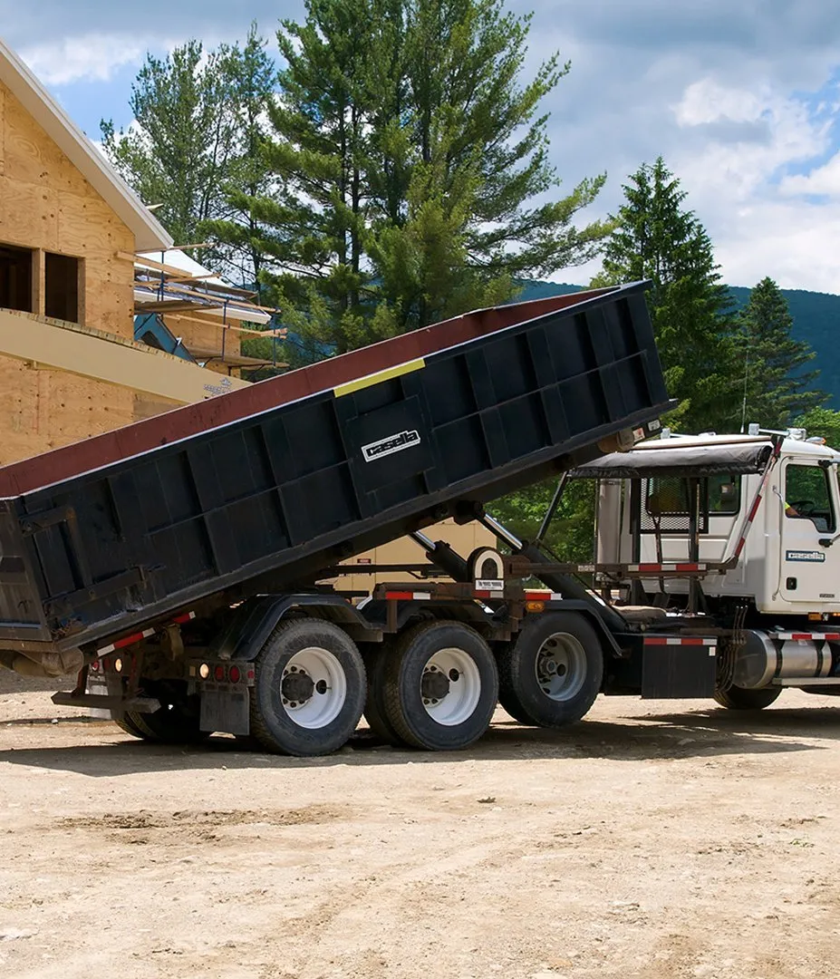 Casella roll-off truck unloading a container at a construction site near a partially built wooden structure. 