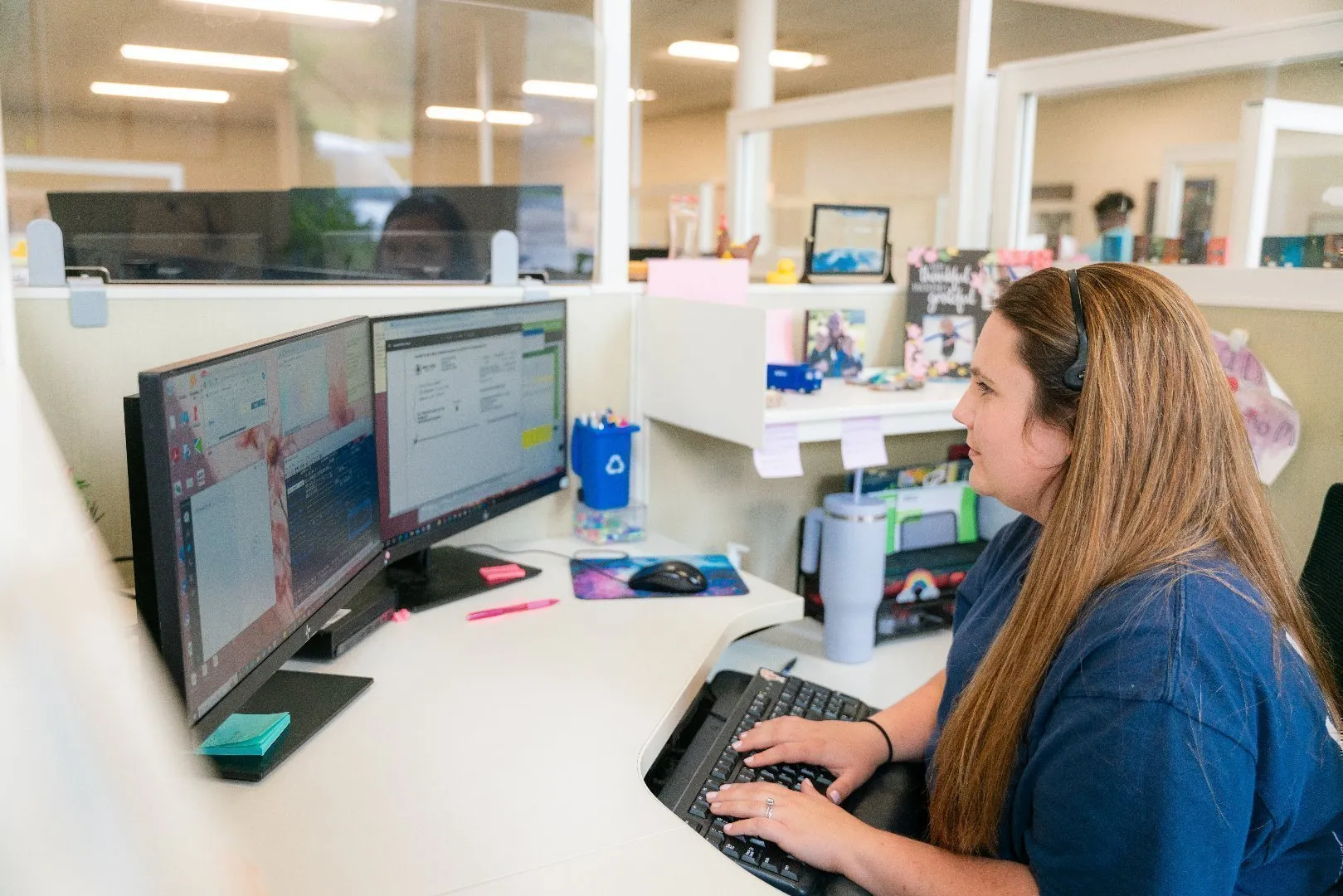 Customer care representative seated at a desk in a modern office cubicle, wearing a headset and typing on a keyboard.