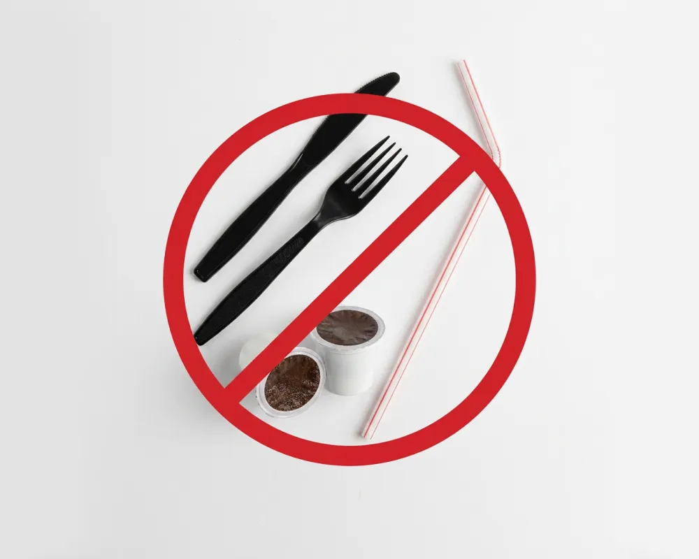 Plastic utensils including a black fork and knife, two small white condiment cups, and a red-striped plastic straw arranged together with a red prohibition symbol over them, indicating these items are not allowed in recycling bins. 