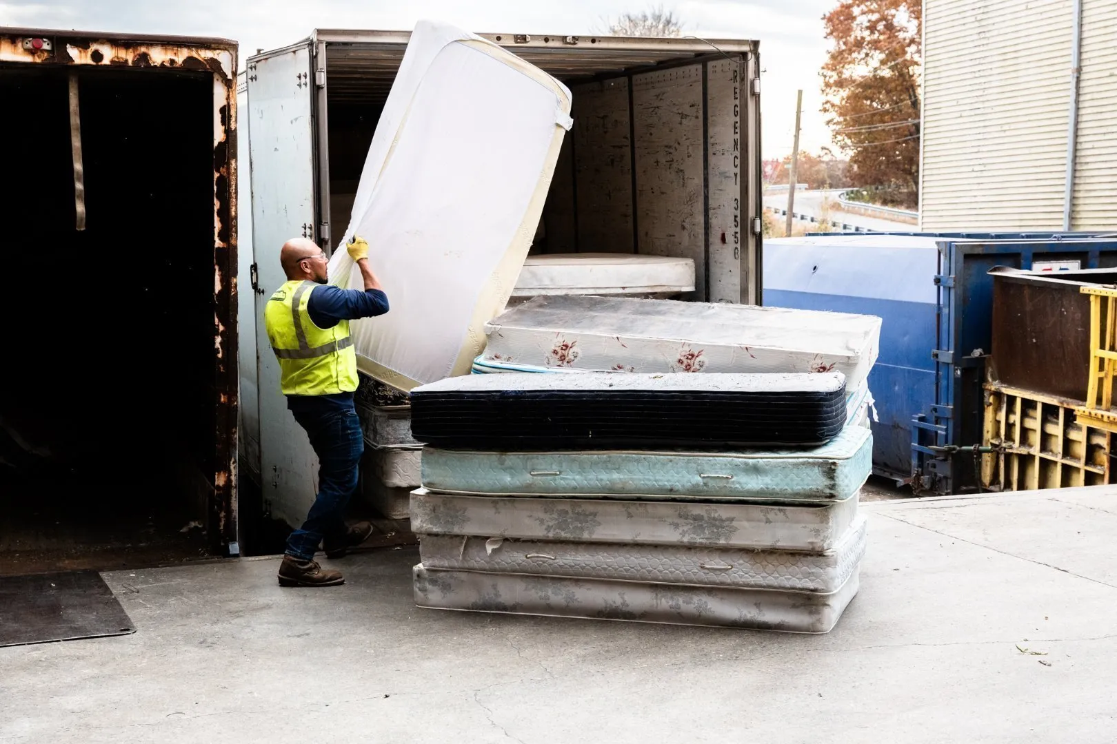 Worker in a safety vest loading a mattress into a container at a recycling facility, showing how bulky materials are collected for proper processing.