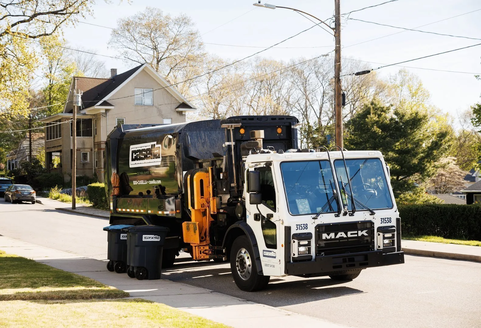 Casella trash and recycling truck collecting residential bins on a suburban street.
