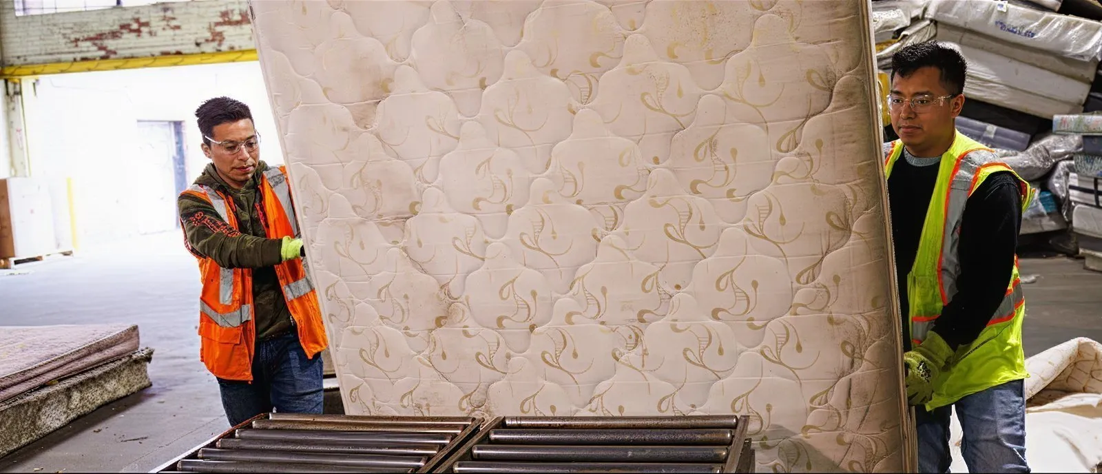 Workers in safety vests handling a large mattress in a recycling facility, demonstrating Casella’s commitment to responsible bulky waste management.