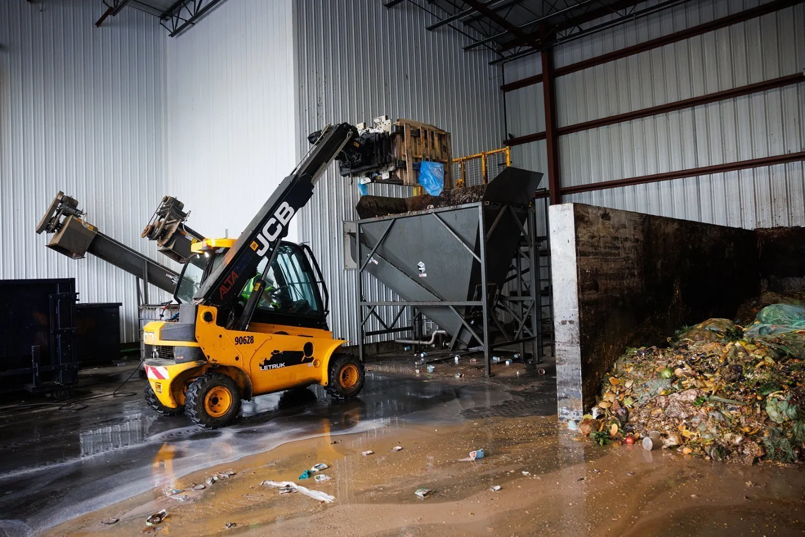 A small yellow forklift loads recycle  materials into a hopper in an recycle facility