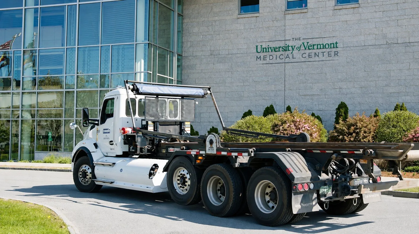 White roll-off truck parked outside the University of Vermont Medical Center building, with the hospital name visible on the stone facade and glass exterior.