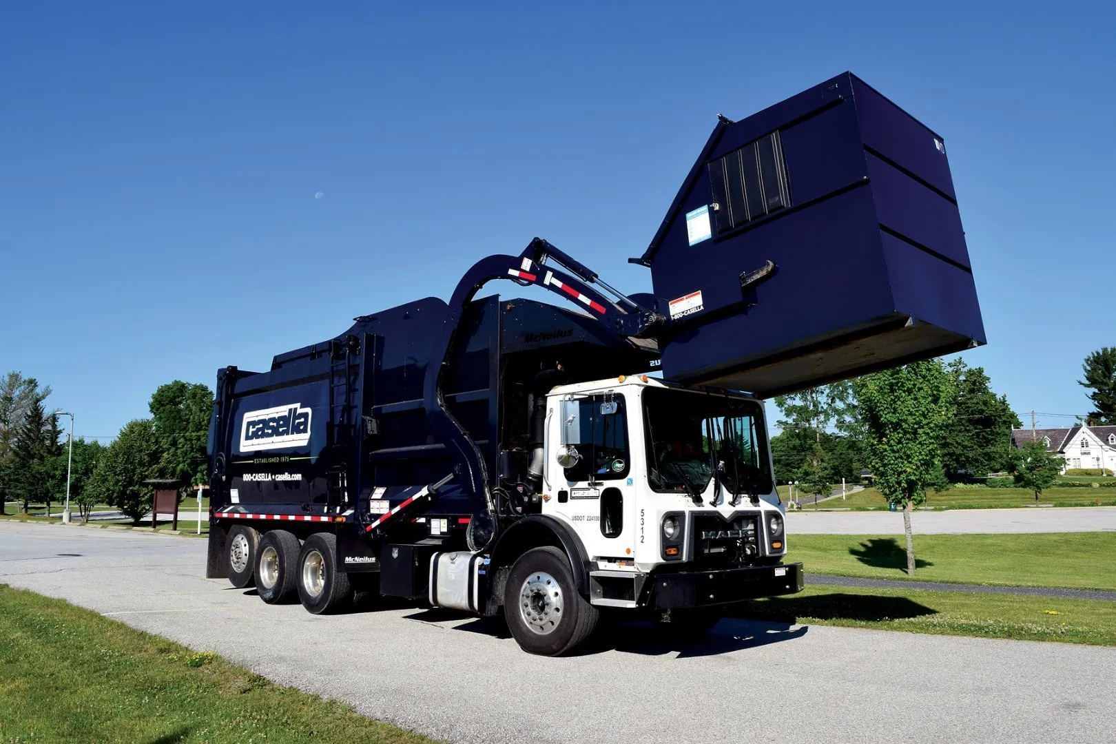 Casella front-load garbage truck lifting a commercial waste bin on a paved road. 