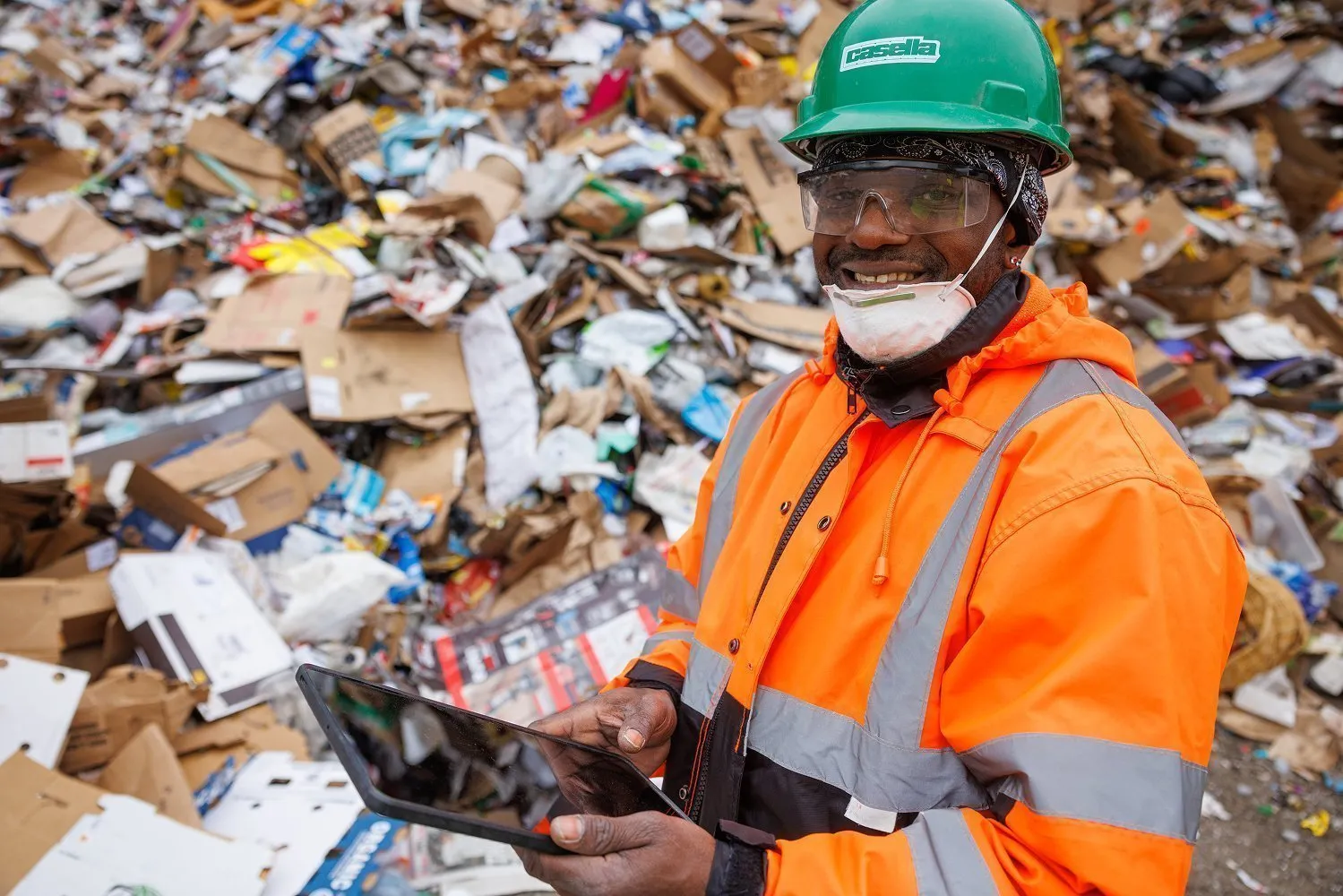 Worker in high‑visibility safety gear assessing a pile of mixed recyclables with a tablet, showing Casella’s commitment to safe, efficient material processing.