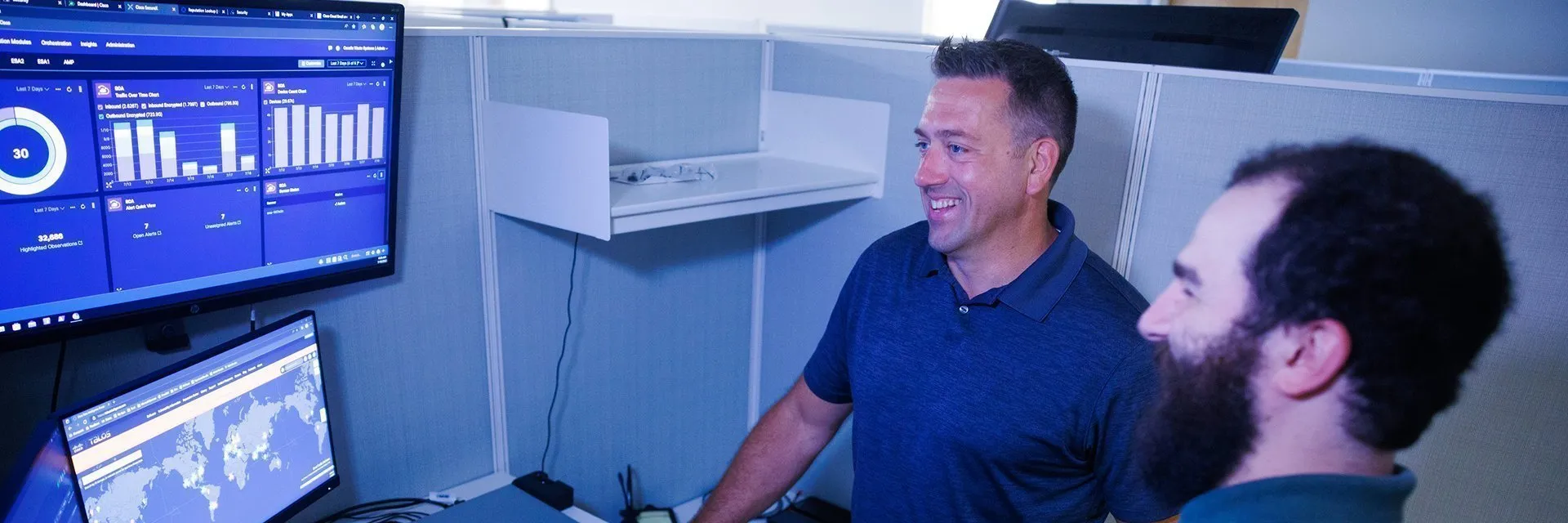 Two colleagues discussing insights from data dashboards displayed on multiple monitors, reflecting Casella’s commitment to technology and operational efficiency.