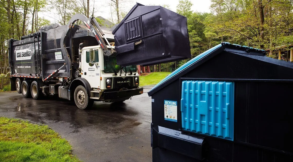 Casella front-load truck lifting a commercial dumpster in front of a university building.