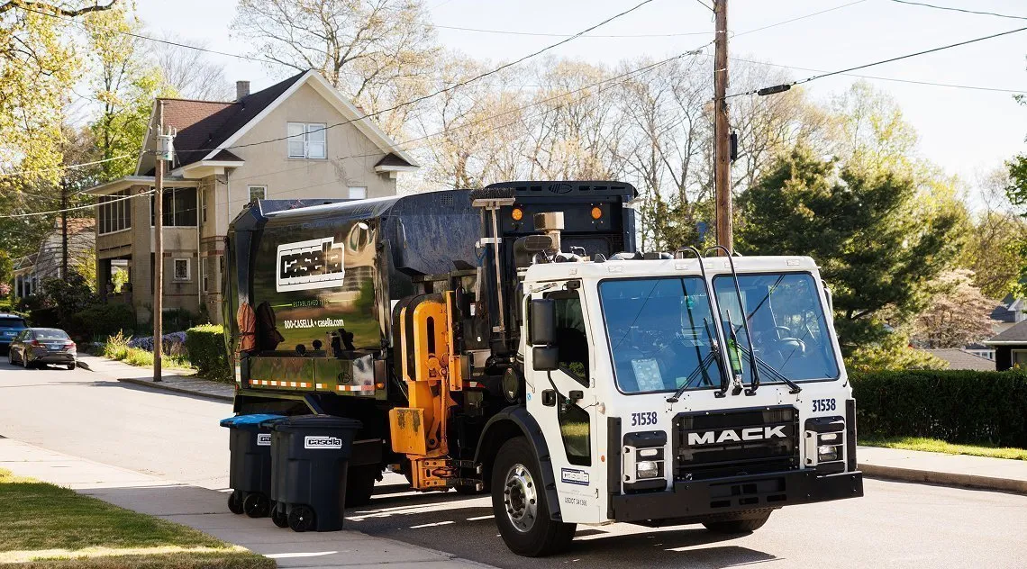 Casella automated side-load truck collecting trash and recycling bins in a residential neighborhood.