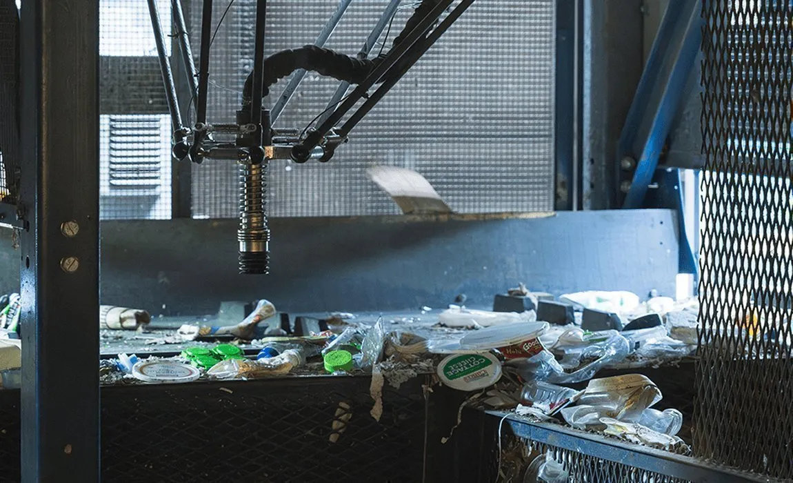 Automated robotic arm sorting recyclable materials on a conveyor belt at a Casella facility.