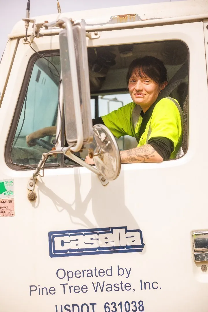 Casella truck cab with company logo on the door, showing a driver wearing a bright yellow safety shirt seated inside.